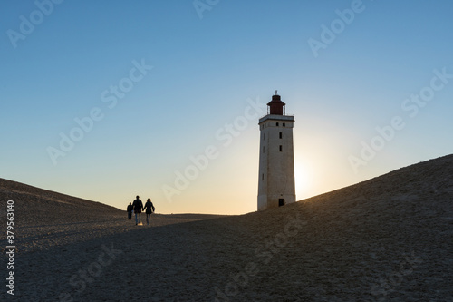 Fototapeta Naklejka Na Ścianę i Meble -  People walking up to Rubjerg Knude lighthouse at sunset