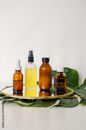 Various amber and matte glass bottles for cosmetics  natural medicine   essential oils or other liquid on a white background standing on a mirror decorated with a green monstera leaf