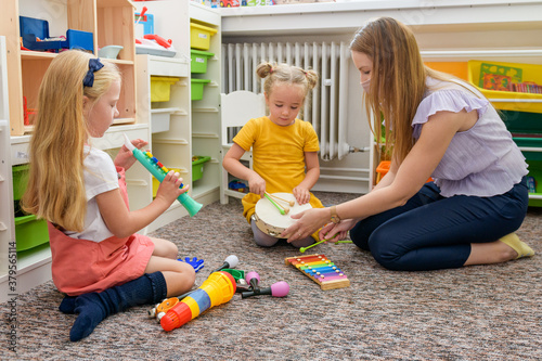 Young female therapist wearing protective face mask playing with two toddler girls during occupational child therapy.
