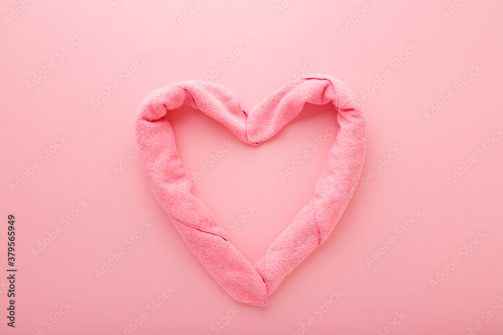 Heart shape created from soft towels on light pink table background. Pastel color. Closeup. Top down view.