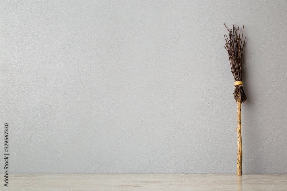 Ancient natural old wooden broom from tree branches for sweeping room, yard and street. Witch broom on floor at gray wall background. Traditional Halloween symbol. Empty place for text. Front view. Ancient natural old wooden broom from tree branches for sweeping room, yard and street. Witch broom on floor at gray wall background. Traditional Halloween symbol. Empty place for text. Front view.