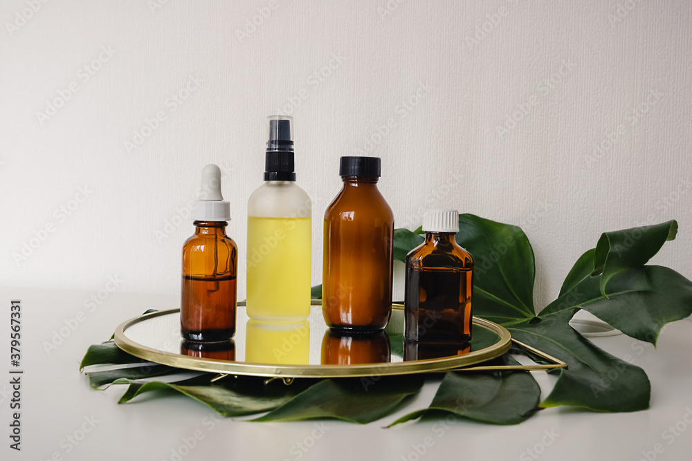 Various amber and matte glass bottles for cosmetics, natural medicine , essential oils or other liquid on a white background standing on a mirror decorated with a green monstera leaf Various amber and matte glass bottles for cosmetics, natural medicine , essential oils or other liquid on a white background standing on a mirror decorated with a green monstera leaf