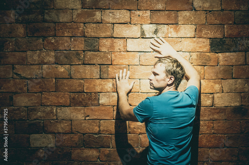 Rear view man under life crisis problems stand facing brown brick wall, hands raised up on wall push sign, wants to climb, overcome obstacle, reach a goal, leader, motivation. Looking left