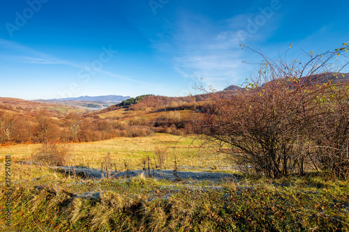 mountainous countryside in november. leafless trees on hills rolling in to the rural valley. snow capped ridge in the distance. sunny morning scenery