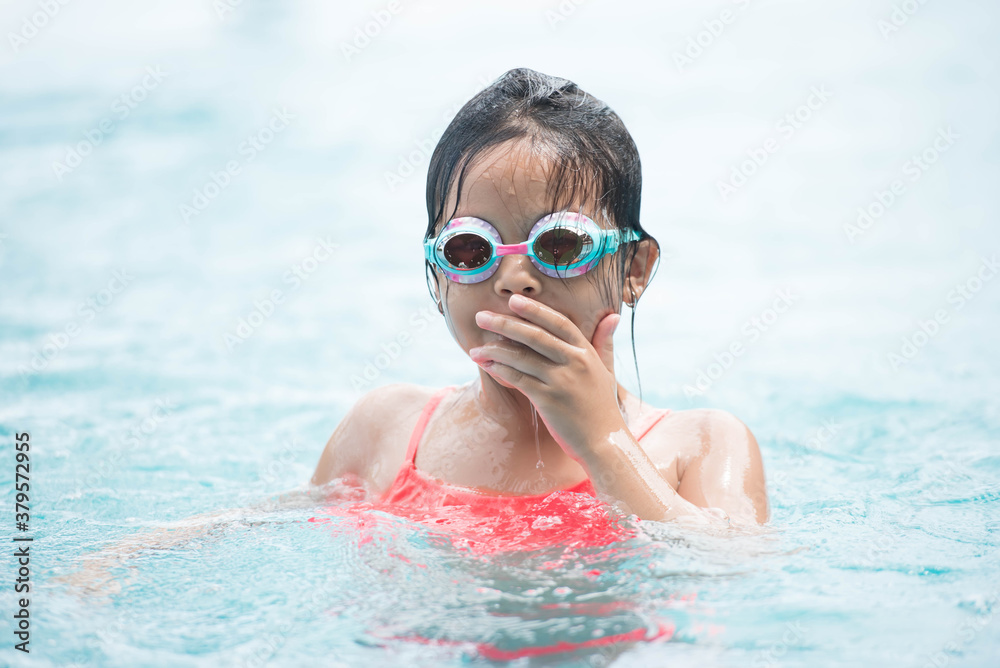 Naklejka premium smiling child wearing swimming glasses in swimming pool. little girl playing in outdoor swimming pool on summer vacation on tropical beach island. child learning to swim in pool of luxury resort.