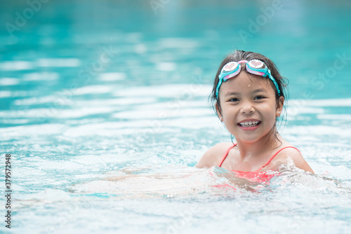 smiling child wearing swimming glasses in swimming pool. little girl playing in outdoor swimming pool on summer vacation on tropical beach island. child learning to swim in pool of luxury resort.