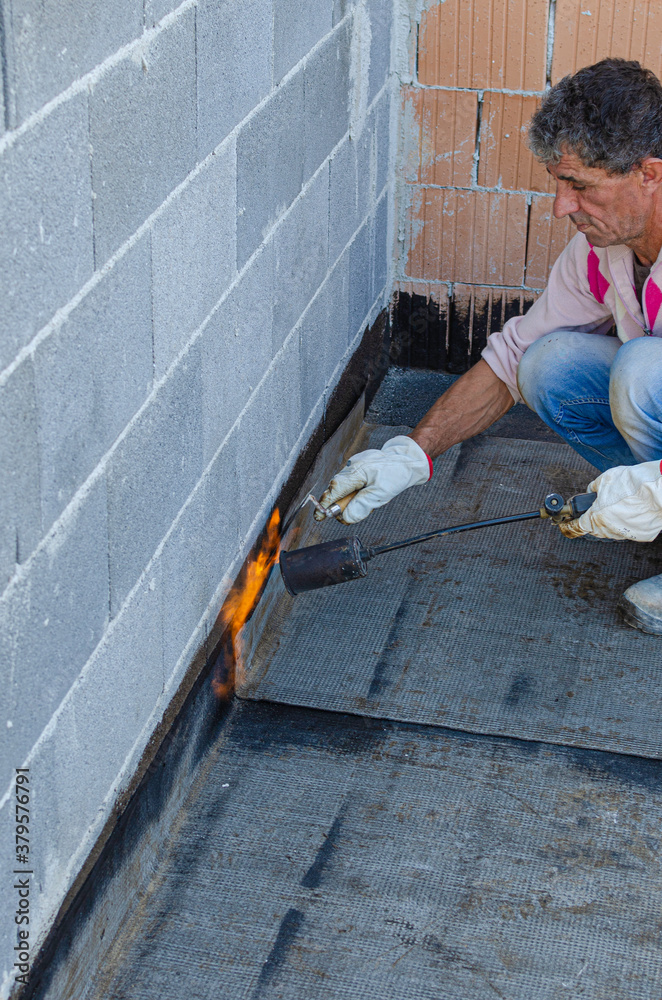 Propane blowtorch at floor slab insulation work. Flat roof covering works with roofing felt Propane blowtorch at floor slab insulation work. Flat roof covering works with roofing felt