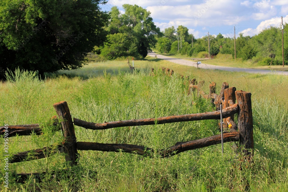 wooden fence in a pasture with green grass and blue sky north of Hutchinson Kansas USA.