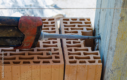 Anchoring of the masonry in the pillar for the anti-seismic prescription. With an electric drill, the hole for anchoring the steel bar to the reinforced concrete structure is made photo