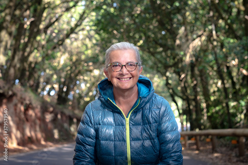 Cheerful smiling senior woman with white hair and glasses enjoying freedom and nature in excursion in the woods