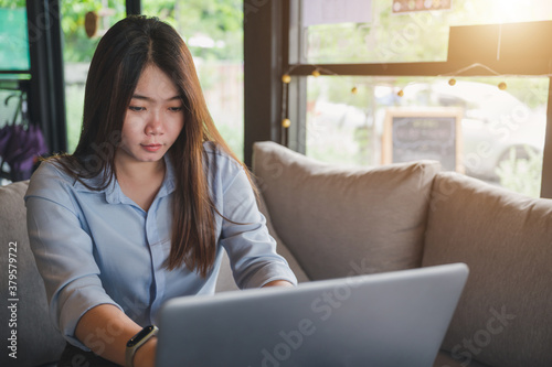 A female Asian office worker of Thai descent is typing and working with notebooks in a coffee shop during the day. She was wearing a blue shirt