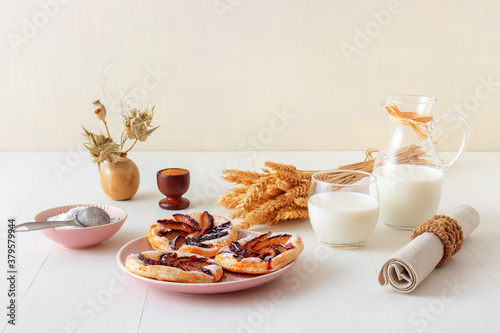 Small plum tarts on plate with cinnamon and icing sugar on white wooden table, delicious puff pastry dessert. photo