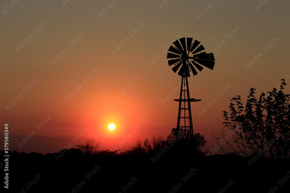 windmill at sunset with tree's,sky and the Sun north of Hutchinson Kansas USA out in the country.