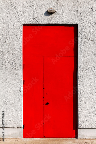 Red metal door in a concrete wall © akintevs