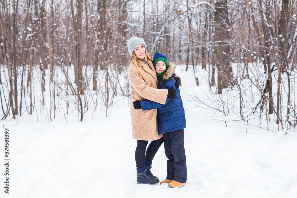Portrait of happy mother with child son in winter outdoors. Snowy park. Single parent.