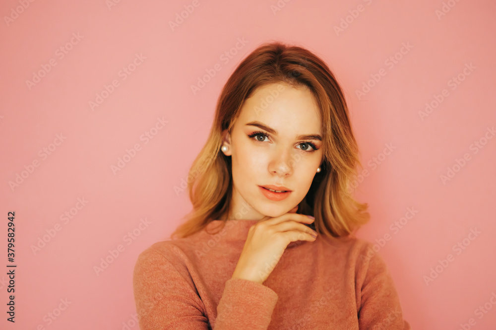 Close photo of a beautiful young woman in a sweater posing on a pink background, seductively looking at the camera. Cute lady isolated on pink. Close photo of a beautiful young woman in a sweater posing on a pink background, seductively looking at the camera. Cute lady isolated on pink.