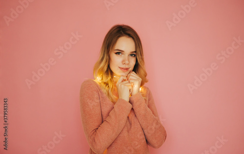 Beautiful lady with a garland in hand poses for the camera on a pink background  looking at the camera with a smile on his face. Christmas concept.