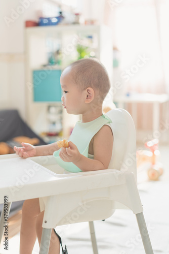 A one-and-a-half-year-old boy eats in a dining chair