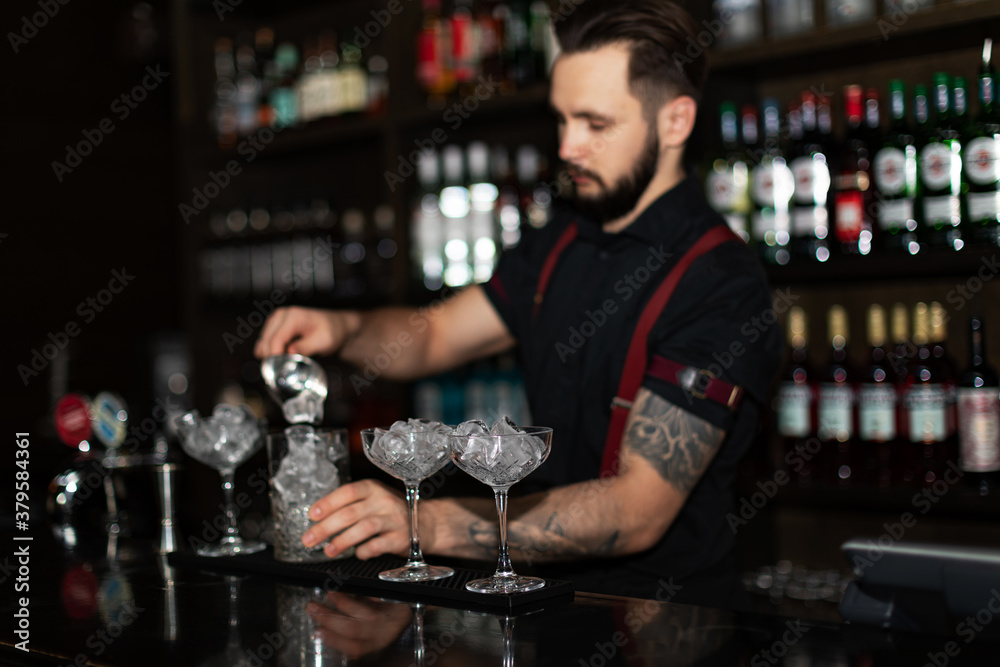 Bartender making refreshing coctail on a bar background. Dark moody style. Ice in the glass. Fosuc on glass