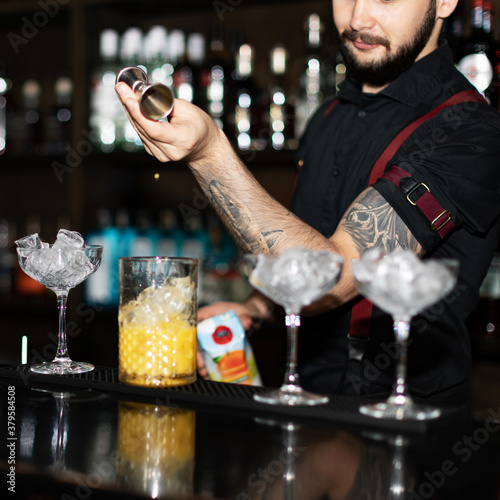 Bartender making refreshing coctail on a bar background. Dark moody style. Ice in the glass. Fosuc on model photo