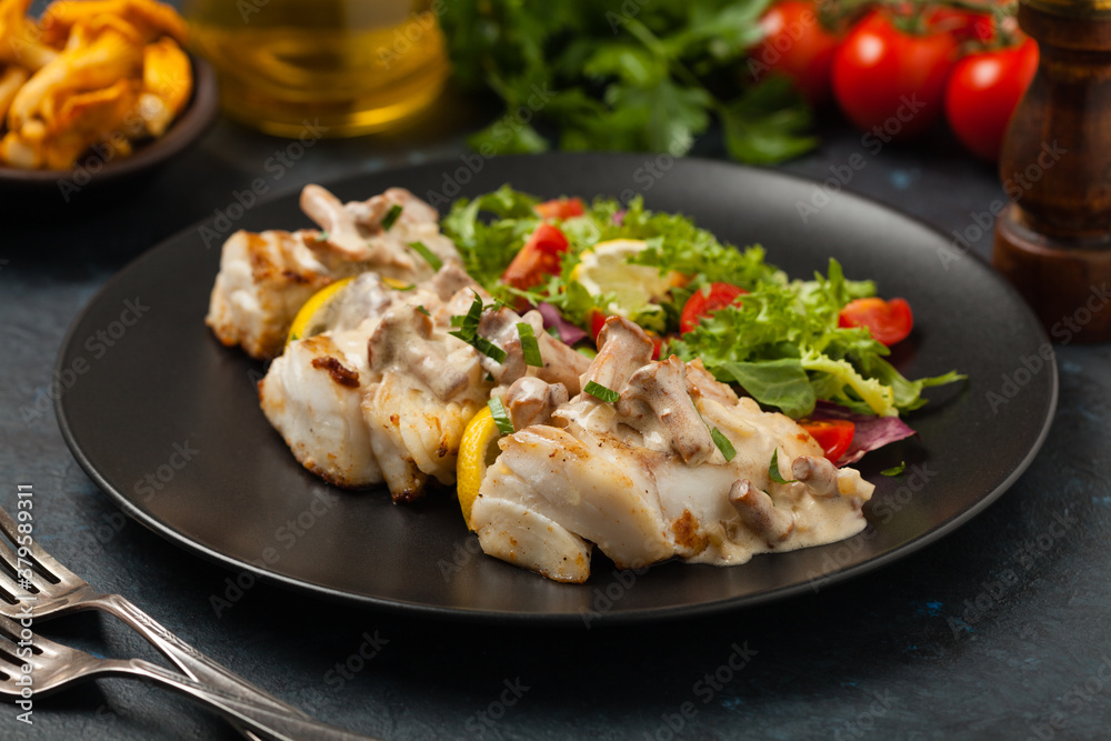 Fried cod served with mushroom sauce and salads. Portion on a black plate. Dark background.