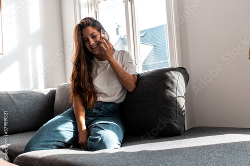 Mujer joven hablando por celular sobre un sofa en tiempos de corona virus - Quedarse en casa - Young woman talking on a cell phone on a sofa in times of coronavirus - Stay home