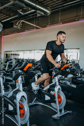 Sporty man riding spinning bikes at gym.