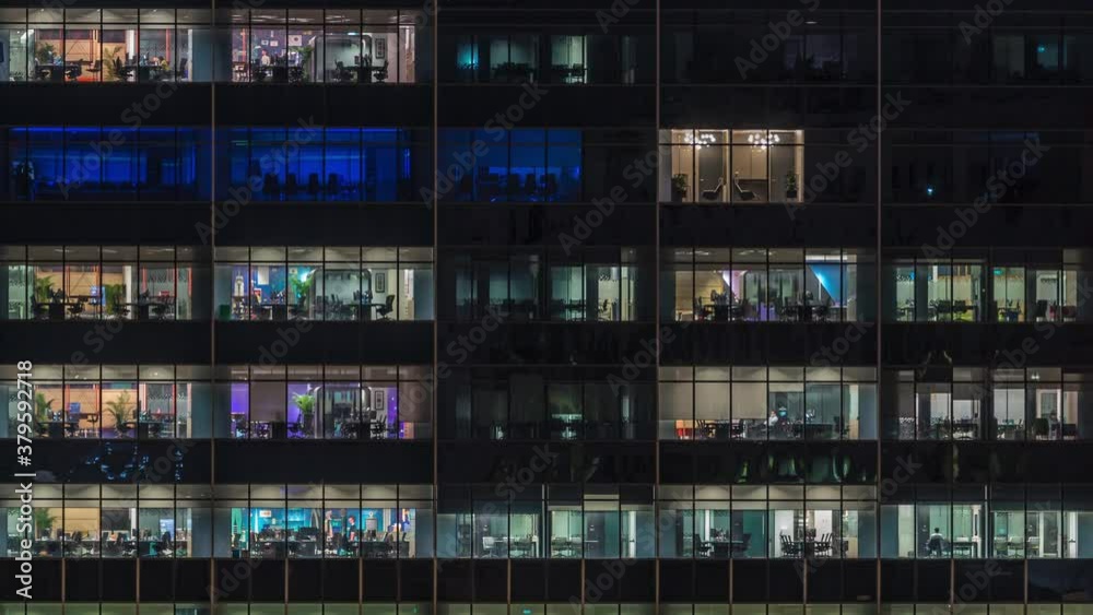 Modern office building with big windows at night timelapse close up view, in windows glowing light shines and some people inside, Singapore. Tilt down Modern office building with big windows at night timelapse close up view, in windows glowing light shines and some people inside, Singapore. Tilt down