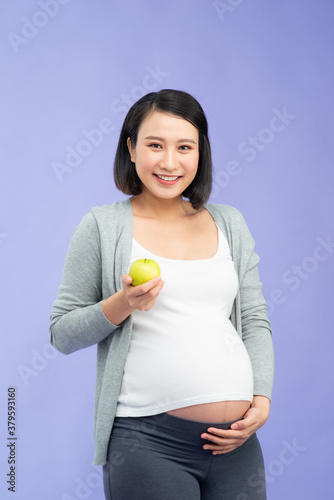 Image of a beautiful young pregnant woman posing isolated over purple wall background holding apple eat healthy food.