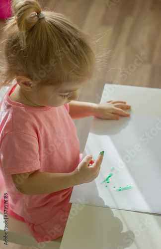 little girl drawing with fingerpaints , dunks his finger in the paints, color finger stamps. photo