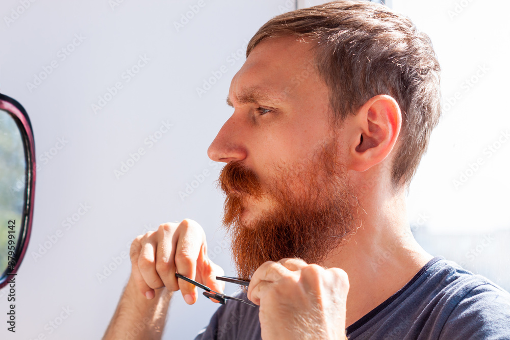 Adult man cutting his own beard and mustache with scissors and comb