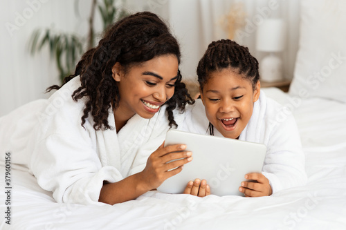 Cheerful Black Mom And Daughter Relaxing On Bed With Digital Tablet