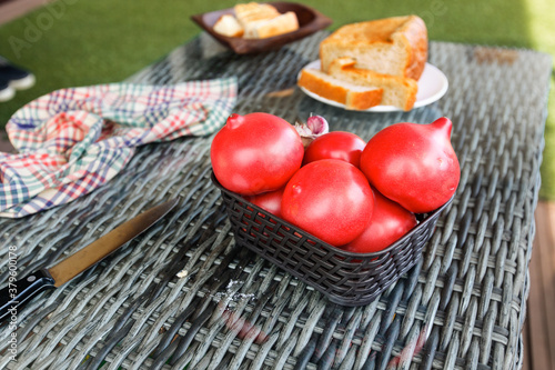 Red ripe tomatoes in basket on wicker table. Cutting knife, kitchen towel,bread as background. Selective focus
