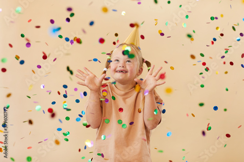 Waist up portrait of excited girl with down syndrome smiling happily while standing under confetti shower in studio, copy space