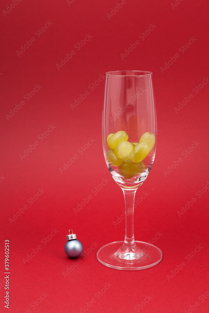 Twelve grapes in a glass for sparkling wine cava. Selective focus, red background, copy space. Spanish traditional to eat twelve 12 berries for good luck at midnigth. Christmas New Year composition