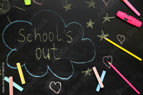 Pieces of color chalk and stationery on blackboard with text School's Out, flat lay. Summer holidays