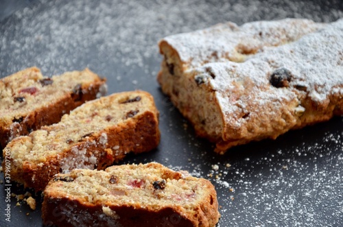 Traditional homemade German Weihnachtsstollen (Christmas stollen or cake) on a slate plate, powdered sugar on top, sliced, filled with candied fruits, raisins, ground almonds and hazelnuts