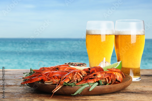Cooked crayfishes served with beer on wooden table near sea