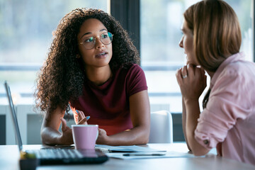 Two beautiful business women working together with laptop while talking about job news in the office.