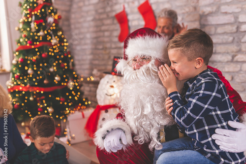 Little boy sitting in Santas lap whispering wishes for Christmas presents