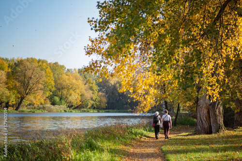 couple walking in autumn park with lake in sunny weather