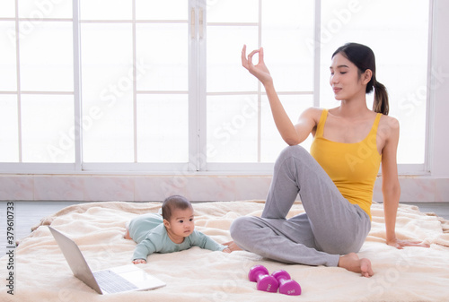 Asian mother workout after delivery newborn baby, young mom watching videos training lose weight yoga sport by computer laptop, beautiful women and toddler infant play together with love and caring
