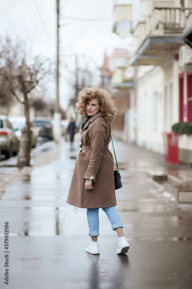 Naklejka premium Portrait of a curly-haired young woman who walks the streets of the city. The girl turns around and smiles
