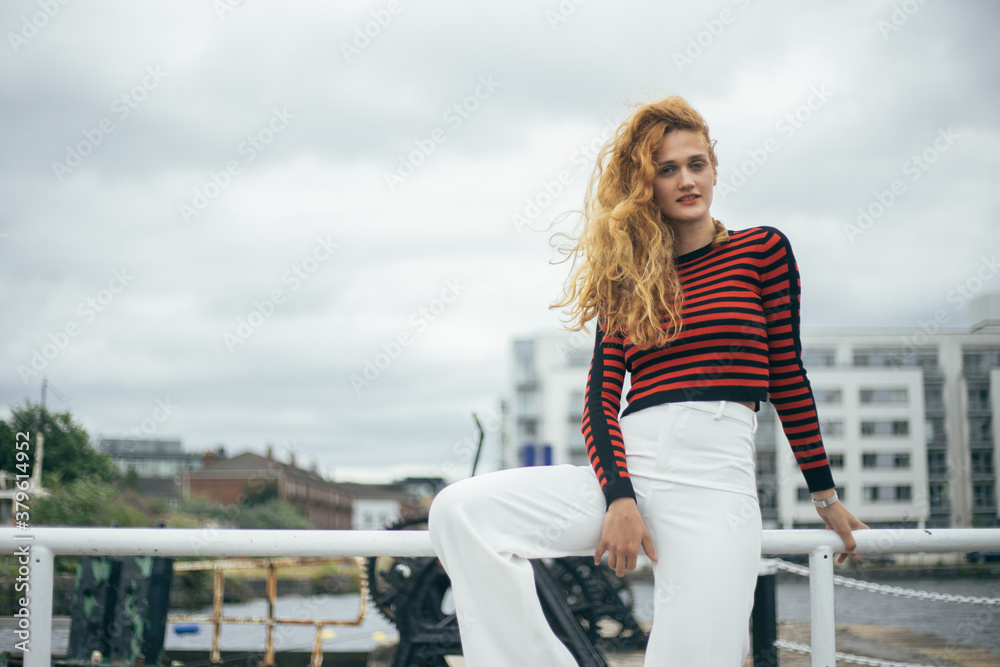 young redhead girl sitting on a fence, urban background with buildings young redhead girl sitting on a fence, urban background with buildings