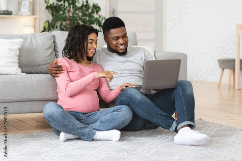 Cheerful pregnant black couple using laptop at home