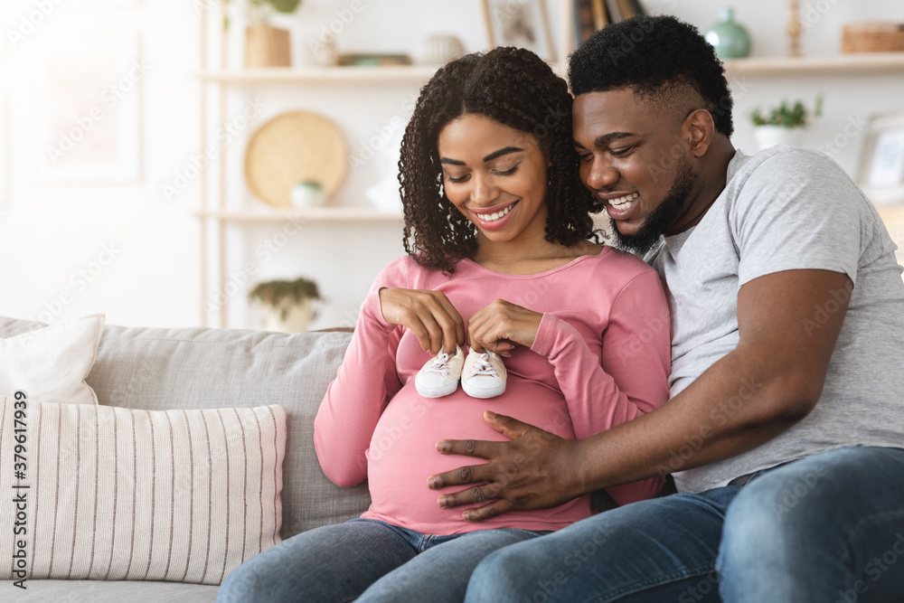 Φωτογραφία Happy black pregnant couple placing baby shoes on woman belly