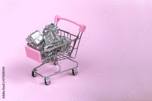 Shopping cart on a pink background with new year and Christmas gifts in silver packaging. Flat lay. Top view. Copy space.