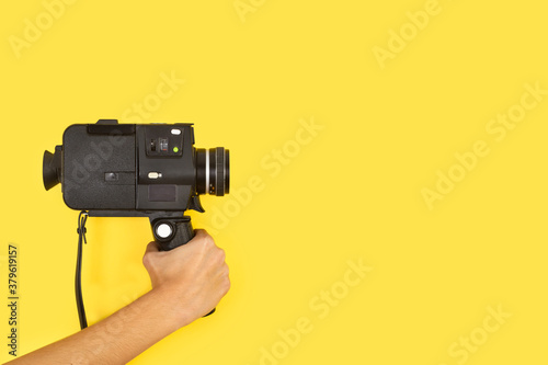 Mano femenina sosteniendo una cámara de película de 8 mm de estilo antiguo sobre un fondo amarillo liso y aislado. Vista de frente. Copy space