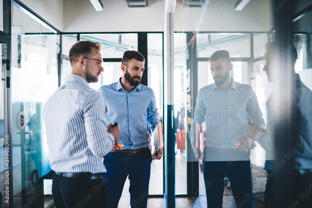 Young 20s male professionals discussing solutions on meeting enjoying productive cooperation, skilled men experts looking at infographic and sketches checking analytic together for startup