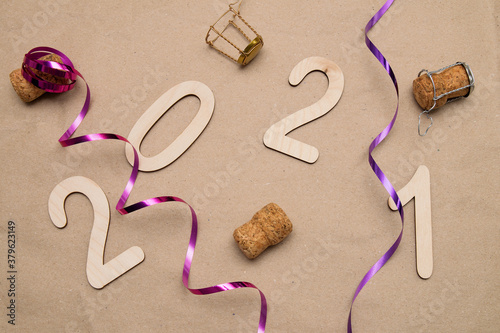 Light wooden 2021 numbers lie randomly on craft paper with champagne corks, packing tape and muzlet photo